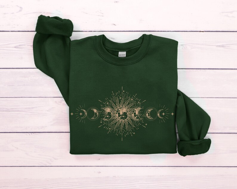 May include: A dark green sweatshirt with a gold sun and moon design. The design features a sun with rays and a crescent moon with stars.