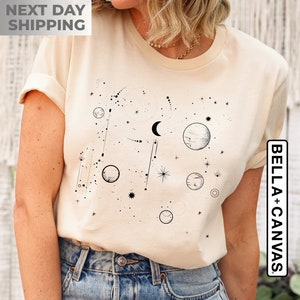 May include: A cream-colored t-shirt with a black and white graphic of a celestial scene with planets, stars, and a crescent moon.