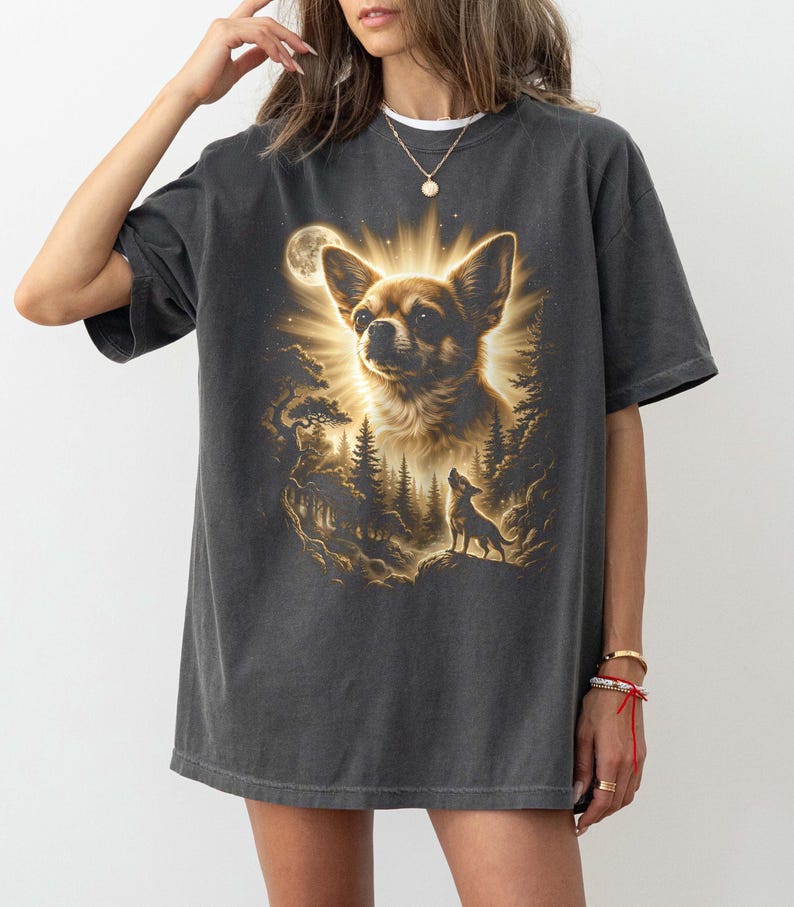 May include: Dark gray t-shirt featuring a detailed illustration of a Chihuahua with a radiant halo, set against a forest and moonlit sky. A smaller dog silhouette is howling. The design is in shades of brown and gold.