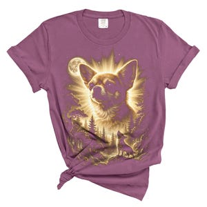 May include: A mauve-colored t-shirt featuring a detailed illustration of a Chihuahua dog with a radiant halo effect, set against a forest and moonlit sky. A smaller dog silhouette is also visible. The shirt has rolled-up sleeves and a knotted hem.