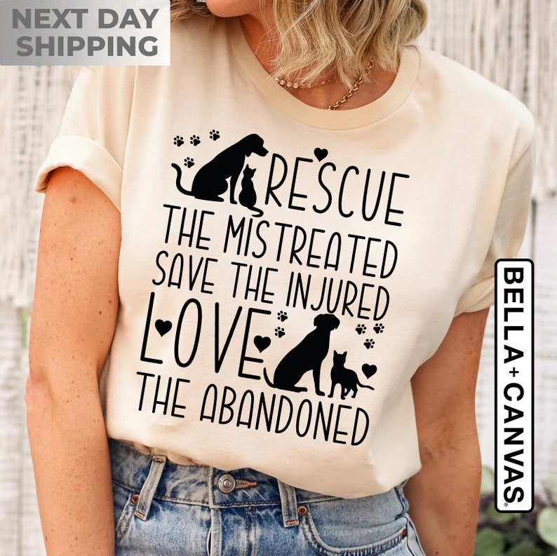 May include: A beige t-shirt with a black graphic design featuring a dog and cat with the text "Rescue the mistreated, save the injured, love the abandoned".