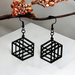 Peut inclure: Une paire de boucles d'oreilles géométriques noires de forme hexagonale avec un design en fil. Les boucles d'oreilles sont suspendues à un crochet argenté.