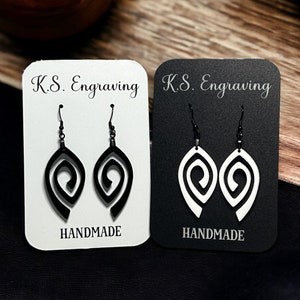 Peut inclure: Deux paires de boucles d'oreilles en spirale noires et blanches présentées sur du papier cartonné blanc et noir. Les cartes portent le texte "K.S. Engraving" et "Handmade" imprimé dessus.