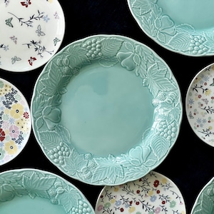 May include: A collection of decorative plates with floral and leaf patterns. The plates are in various colors, including white, blue, and green. The plates are arranged in a circular pattern on a black background.