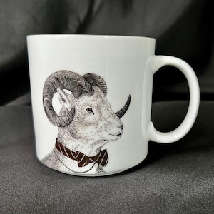 May include: White ceramic mug with a black and white illustration of a ram wearing a bow tie. The ram has large curled horns and a detailed face.