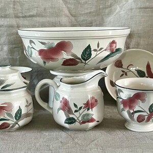 May include: A set of white ceramic kitchenware with a floral design featuring pink and green flowers. The set includes a large bowl, a creamer, a sugar bowl, a teacup, and a saucer.