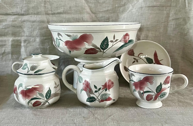 May include: A set of white ceramic kitchenware with a floral design featuring pink and green flowers. The set includes a large bowl, a creamer, a sugar bowl, a teacup, and a saucer.