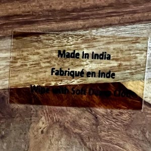 Op de afbeelding: Close-up van een bruin houten oppervlak met een doorzichtig acryl label waarop "Made in India" en "Fabriqu&eacute; en Inde" staat.