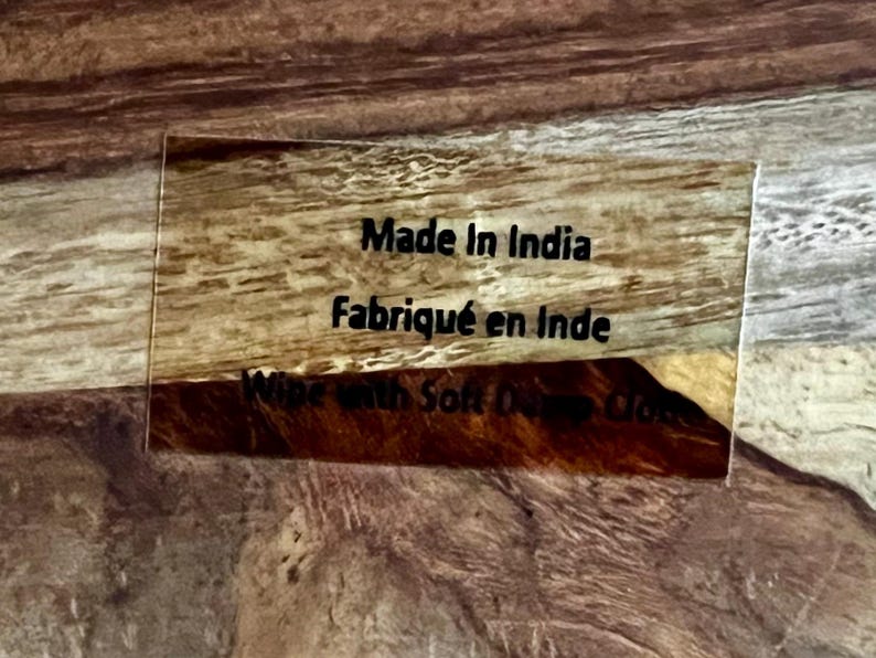 Op de afbeelding: Close-up van een bruin houten oppervlak met een doorzichtig acryl label waarop "Made in India" en "Fabriqu&eacute; en Inde" staat.
