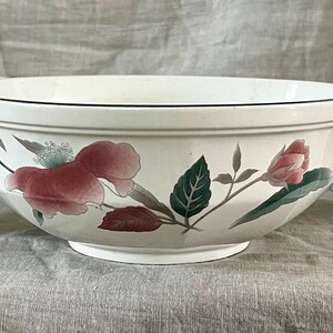 May include: A set of white ceramic bowls with a floral design featuring pink flowers and green leaves. The bowls are in various sizes and shapes, including a large serving bowl and smaller individual bowls.