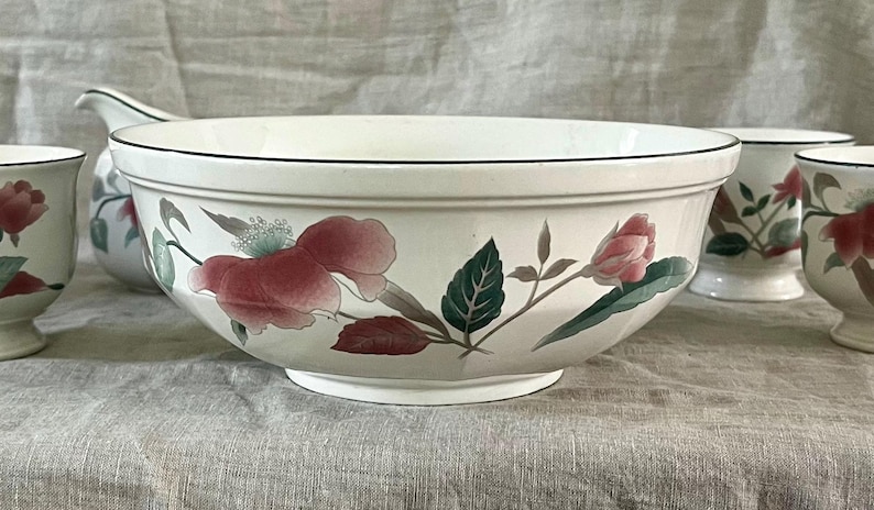 May include: A set of white ceramic bowls with a floral design featuring pink flowers and green leaves. The bowls are in various sizes and shapes, including a large serving bowl and smaller individual bowls.