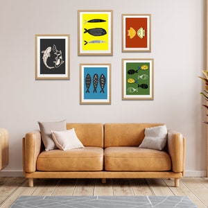 Peut inclure: Cinq impressions encadrées d'illustrations de poissons. Les impressions sont de couleurs et de styles différents et sont disposées en grille sur un mur blanc. Les impressions sont toutes encadrées dans des cadres en bois naturel.