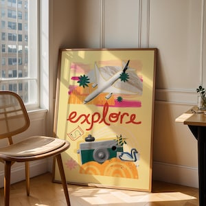 May include: A framed poster with the word "explore" in red script. The poster features a white airplane, a green camera, and a white swan on a yellow background. The poster is leaning against a wall next to a wooden chair.