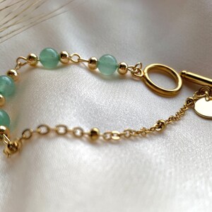 Peut inclure: Un bracelet en chaîne dorée avec des perles vertes et un fermoir à glissière. Le bracelet est doté d'un petit charme rond attaché au fermoir.