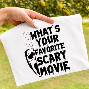 May include: A white ceramic mug with a black handle and the text "But First, Coffee" in a bold, black font. The mug is filled with a dark liquid, likely coffee, and sits on a light-colored surface.