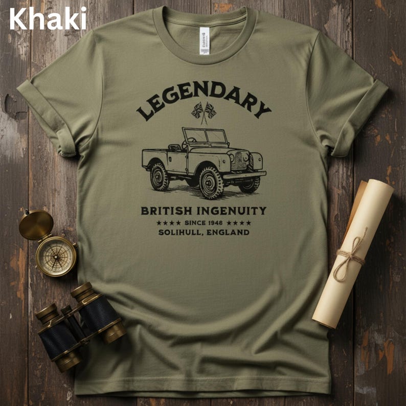 Puede incluir: Camiseta caqui con un gr&aacute;fico de coche antiguo y el texto "LEGENDARY BRITISH INGENUITY SINCE 1948 SOLIHULL, ENGLAND." La camiseta se muestra con una br&uacute;jula, unos prism&aacute;ticos y un pergamino enrollado sobre una superficie de madera.
