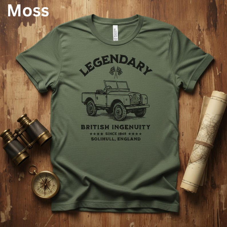 Puede incluir: Camiseta verde musgo con un gr&aacute;fico negro de un veh&iacute;culo todoterreno vintage. El texto sobre el veh&iacute;culo dice "LEGENDARY", y debajo, "BRITISH INGENUITY SINCE 1948 SOLIHULL, ENGLAND". La camiseta se muestra con una br&uacute;jula, binoculares y un mapa.