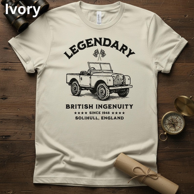 Puede incluir: Camiseta color marfil con una ilustraci&oacute;n negra de un veh&iacute;culo todoterreno vintage. El texto sobre el veh&iacute;culo dice "LEGENDARY", y debajo, "BRITISH INGENUITY SINCE 1948 SOLIHULL, ENGLAND". Tambi&eacute;n hay dos peque&ntilde;as banderas brit&aacute;nicas.