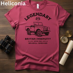 Puede incluir: Camiseta granate con una ilustraci&oacute;n negra de un veh&iacute;culo todoterreno vintage y la palabra "LEGENDARY" encima. El texto "BRITISH INGENUITY" y "SINCE 1948" est&aacute;n debajo. El texto "SOLIHULL, ENGLAND" tambi&eacute;n est&aacute; en la camiseta.