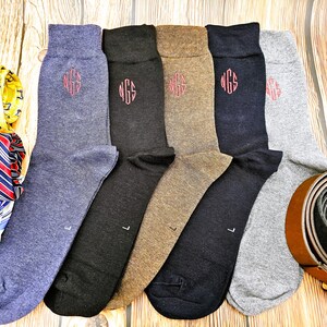 May include: Six pairs of socks in different colors, including gray, brown, black, and blue. Each sock has a monogram embroidered on the top in red thread. The monogram is "NGS".