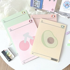 May include: Three pink, yellow, and green gridded memo pads with cute illustrations of a cherry, avocado, and a dog. Each pad has a space for a date and notes.