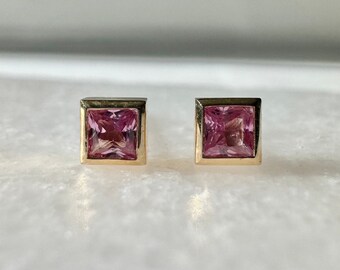 May include: A pair of gold earrings with square pink gemstones.