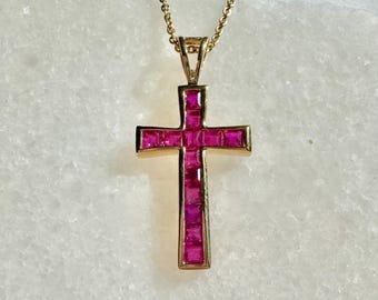 Könnte beinhalten: Eine goldene Kettenkette mit einem Rubin-Kreuz-Anhänger. Das Kreuz besteht aus kleinen quadratischen Rubinen, die in Gold gefasst sind.