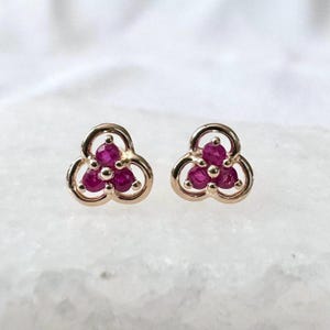 May include: A pair of gold earrings with a clover design. Each earring has three ruby stones set in the centre of the clover.