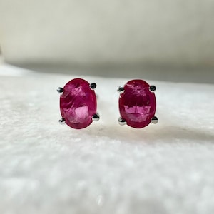 May include: A pair of silver stud earrings with oval-shaped ruby gemstones.