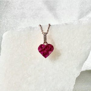 May include: A rose gold necklace with a heart-shaped pendant. The pendant is made of faceted ruby stones and is surrounded by a halo of small diamonds.