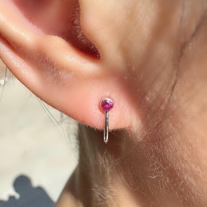 May include: A close-up of a person's ear with a small silver hoop earring featuring a pink gemstone.