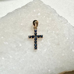 May include: A gold cross pendant with a blue sapphire stone design.