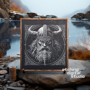 Könnte beinhalten: Eine schwarze, gerahmte Tafel mit einer weißen Gravur eines Wikingerkriegers, der einen gehörnten Helm trägt. Das Gesicht des Kriegers ist mit Bart und Schnurrbart detailliert. Der Hintergrund der Gravur ist ein kreisförmiges Design mit komplizierten Details. Der Text "etching digital studio" ist in Weiß am unteren Rand der Tafel gedruckt.