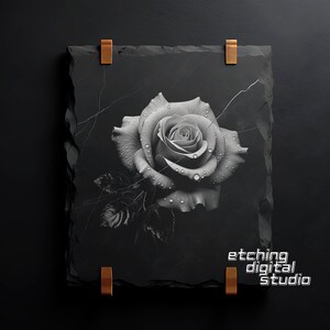 May include: A black and white photograph of a single rose with water droplets on the petals. The rose is printed on a black slate tile with a rough texture. The tile has two copper clips on the top and bottom. The text "etching digital studio" is printed on the bottom right corner of the tile.
