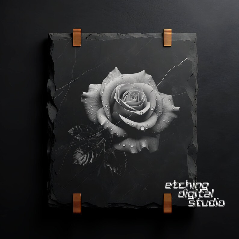 May include: A black and white photograph of a single rose with water droplets on the petals. The rose is printed on a black slate tile with a rough texture. The tile has two copper clips on the top and bottom. The text "etching digital studio" is printed on the bottom right corner of the tile.