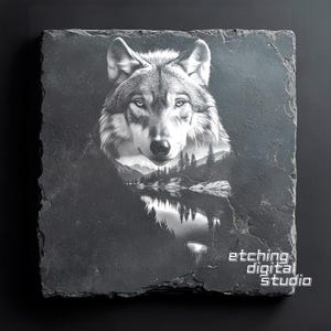 May include: A black and white image of a wolf's head with a forest and lake reflected in its eyes. The image is etched onto a black slate tile with the text "etching digital studio" in the bottom right corner.