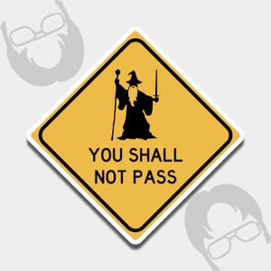 May include: A yellow diamond-shaped sticker with a black silhouette of a wizard holding a staff and sword. The text "YOU SHALL NOT PASS" is printed in black below the wizard image. The sticker has a white border.