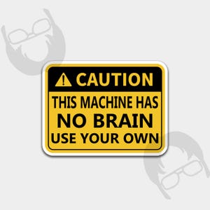 May include: A rectangular sticker with a yellow background and black border. The sticker has the word "CAUTION" at the top, followed by "THIS MACHINE HAS NO BRAIN USE YOUR OWN" in bold, black text. A black triangle with an exclamation point is at the top.