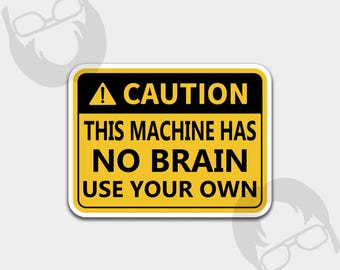 May include: A rectangular sticker with a yellow background and black border. The sticker has the word "CAUTION" at the top, followed by "THIS MACHINE HAS NO BRAIN USE YOUR OWN" in bold, black text. A black triangle with an exclamation point is at the top.