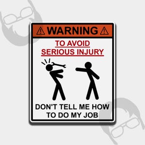 Op de afbeelding: Een rechthoekig bord met een zwarte rand en witte achtergrond. Het bovenste gedeelte is oranje met het woord "WARNING" en een uitroepteken. De tekst luidt "TO AVOID SERIOUS INJURY" en "DON'T TELL ME HOW TO DO MY JOB". Er zijn stokfiguren.