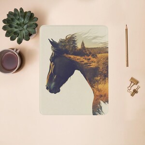 May include: A black horse's head with a forest scene superimposed over it. The horse's mane is flowing in the wind. The background is a blurred image of a field and trees.