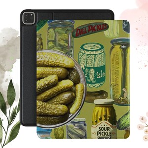 May include: A green and white illustrated iPad case with a pattern of pickles in jars and a bowl of pickles. The text "Dill Pickles" and "Sour Pickle Surprise" are on the case.