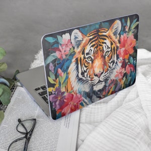 Puede incluir: Una piel para portátil con una ilustración colorida de un tigre rodeado de flores. El tigre es naranja, negro y blanco, y las flores son rosas, moradas y verdes.