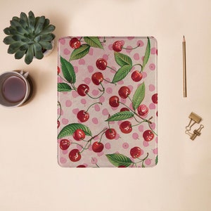 May include: A pink and white patterned notebook cover with a repeating design of red cherries and green leaves.