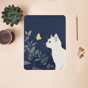 May include: A white cat with blue eyes looks at a yellow butterfly on a dark blue background with green leaves.