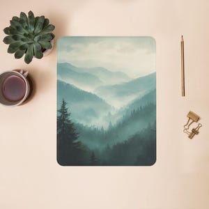 May include: A misty mountain landscape with a forest of evergreen trees in the foreground. The mountains are covered in fog and the sky is a soft blue.