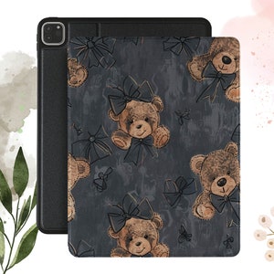 May include: Black iPad case with a cover featuring a pattern of brown teddy bears with dark blue bows on a dark gray background. The case is designed to protect the iPad and add a decorative touch.