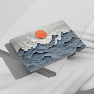 May include: A laptop skin with a blue and white mountain range design and a large orange sun in the upper center of the image.