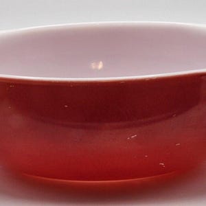 May include: A red and white vintage Pyrex mixing bowl with a white interior and a red exterior. The bowl has a rounded shape and a smooth surface.