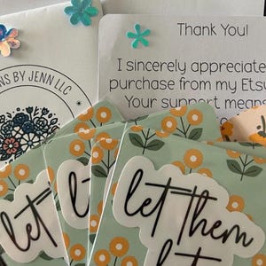 Puede incluir: Un conjunto de cuatro pegatinas con un dise&ntilde;o floral y el texto "let them" en letras negras. Las pegatinas est&aacute;n sobre un fondo blanco con un borde verde.